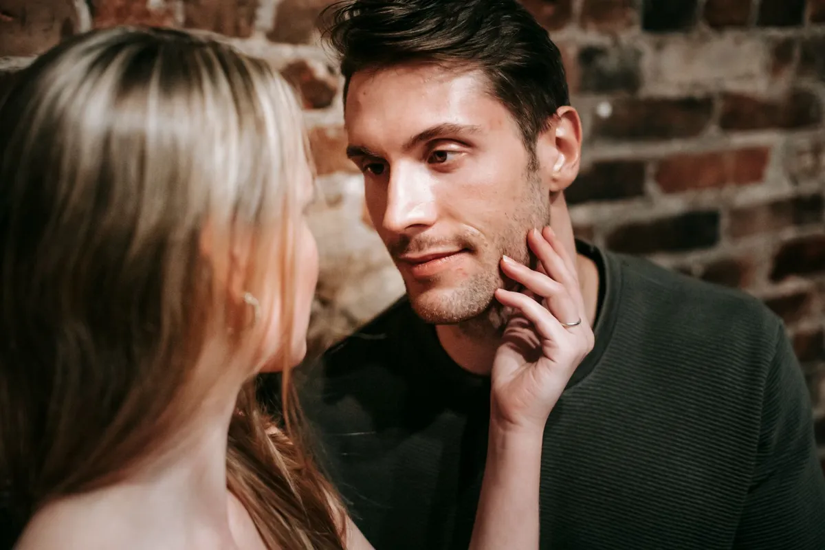 Jeune blonde caressant le visage de son ami lors d'un rendez-vous romantique près d'un mur de briques