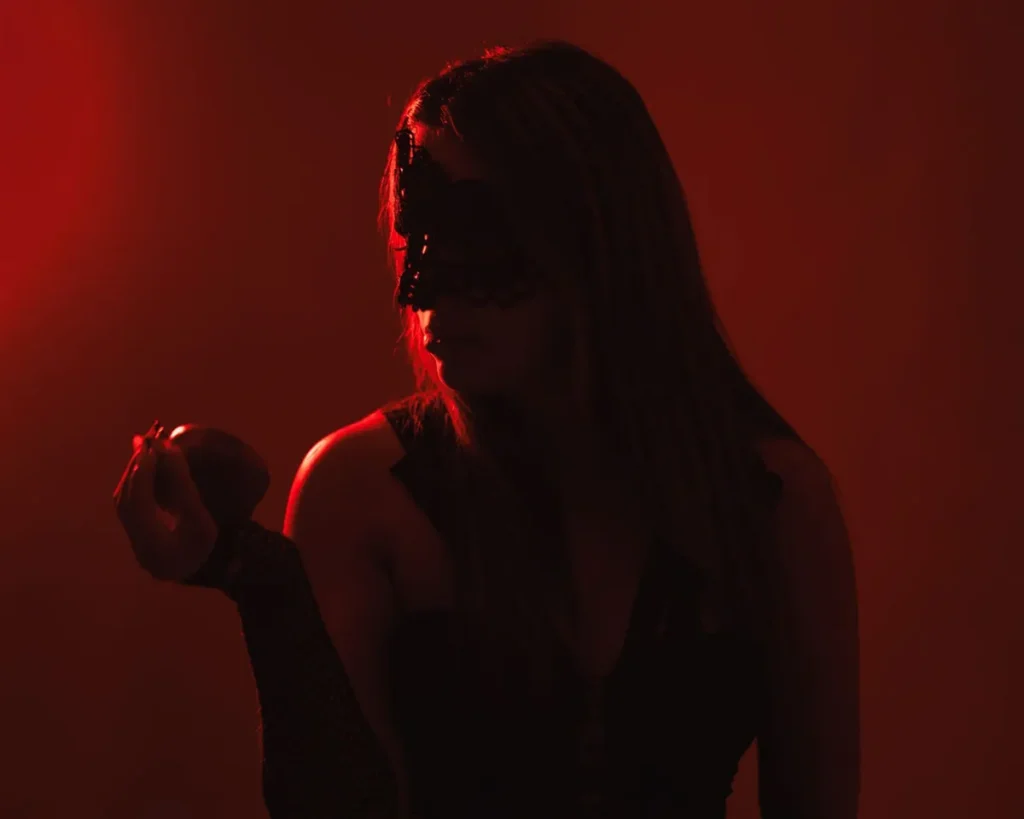 Une femme mystérieuse masquée de noir tient une pomme sous un éclairage rouge