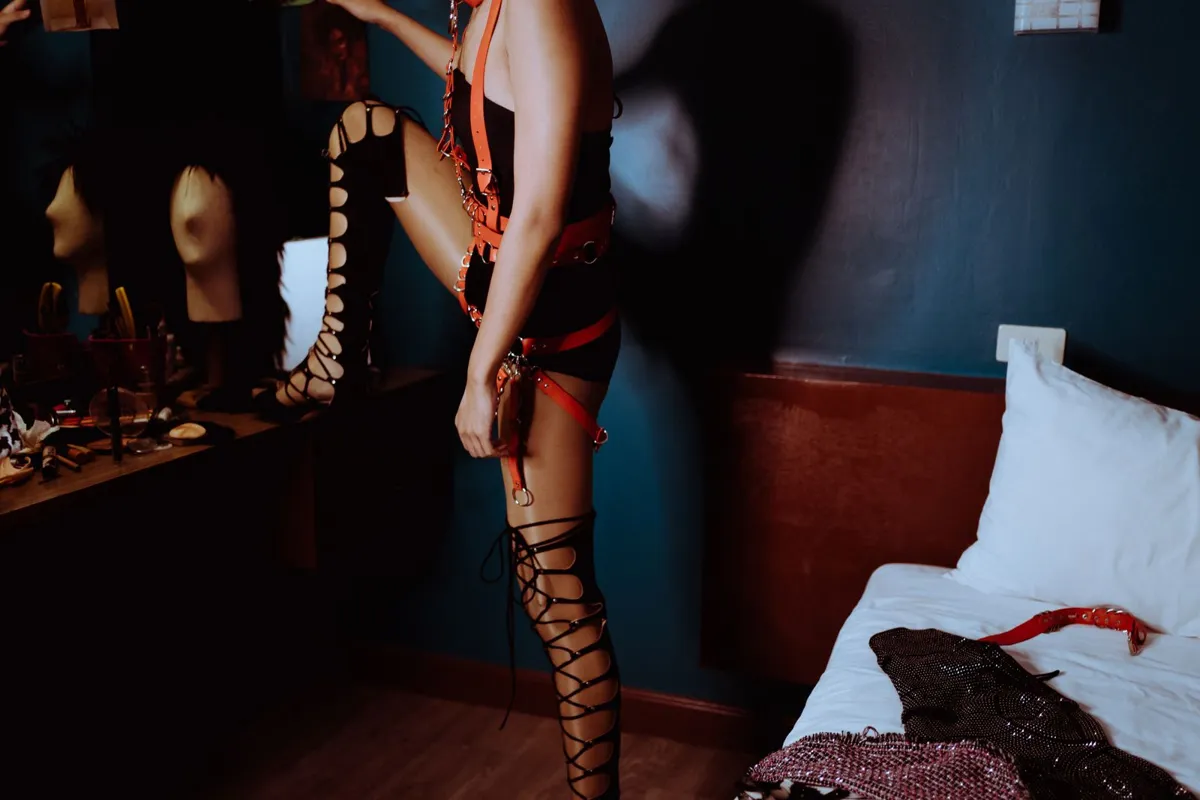 Vue de côté d'un homme trans en harnais BDSM excentrique debout dans une chambre